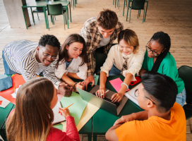 Students sitting around a laptop at a table